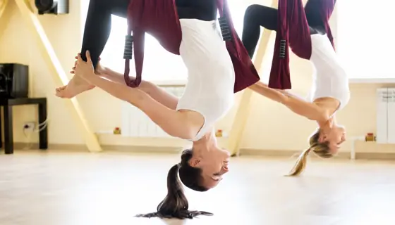 Two women performing aerial yoga upside down in a studio.