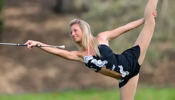 Blonde woman in black outfit performing a baton twirling calisthenics routine outdoors.