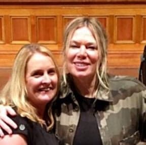 Two blonde women smiling, one wearing a camouflage jacket, on the Dancesurance About Us page.