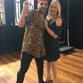 Man in tiger print shirt and woman in black dress at a dance event.