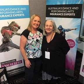 Two women stand smiling next to banners from DanceSurance, insurance experts for performing arts.