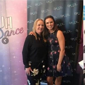 Two women, possibly dancers, pose smiling for a photo against a pink and black DanceSurance backdrop.